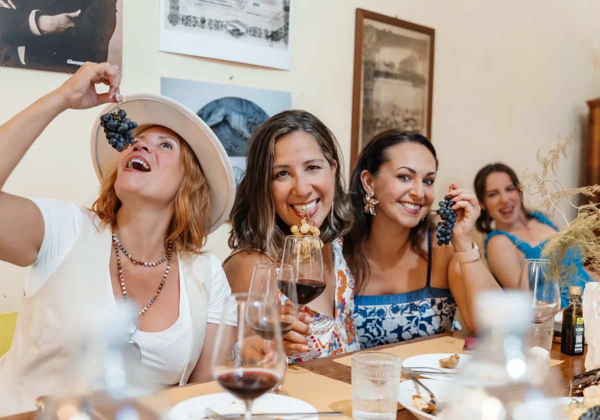 Three retreat guests laughing over wine and a bunch of grapes at the winery